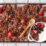 Small batch chocolate granola on a baking sheet with fresh berries.